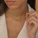 Close-up of a gold bar necklace with a personalized birth flower design and a name engraved as the flower's stem, worn by a woman.