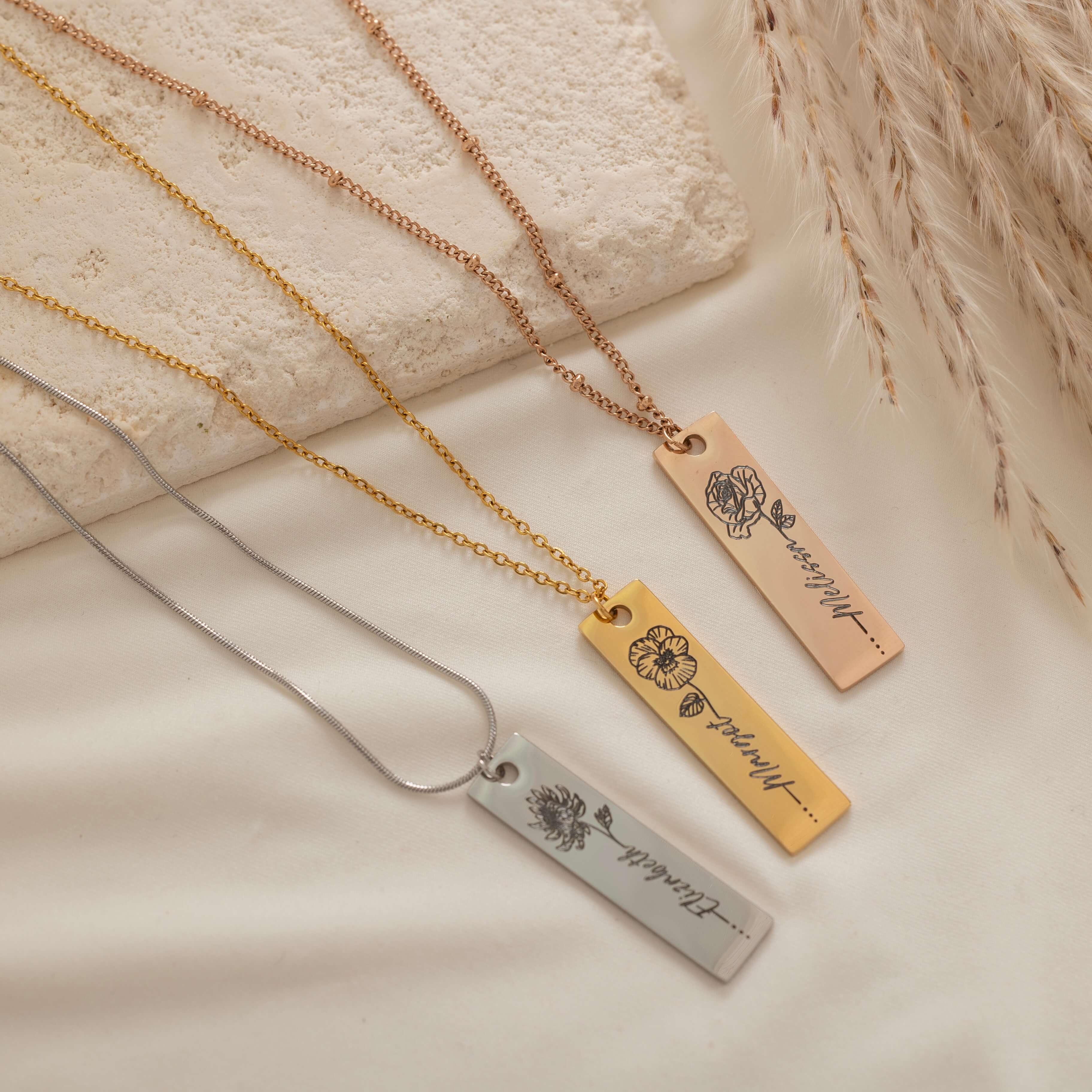 Close-up of a pendant necklaces featuring an engraved birth flower with a personalized name as the stem.