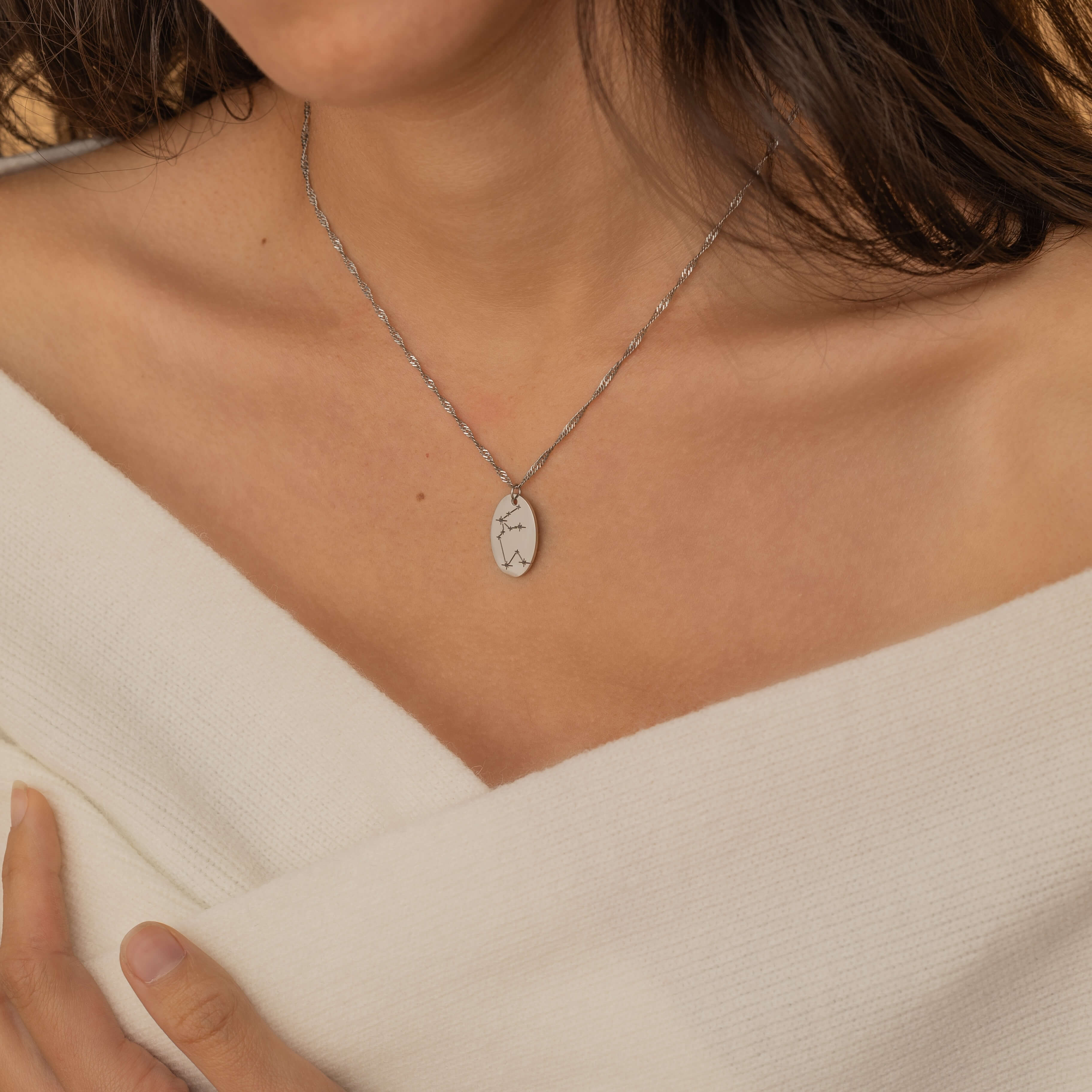 Close-up of a silver pendant necklace featuring an engraved zodiac constellation design.