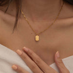 Close-up of a gold pendant necklace engraved with a dog's ear outline, worn by a woman.