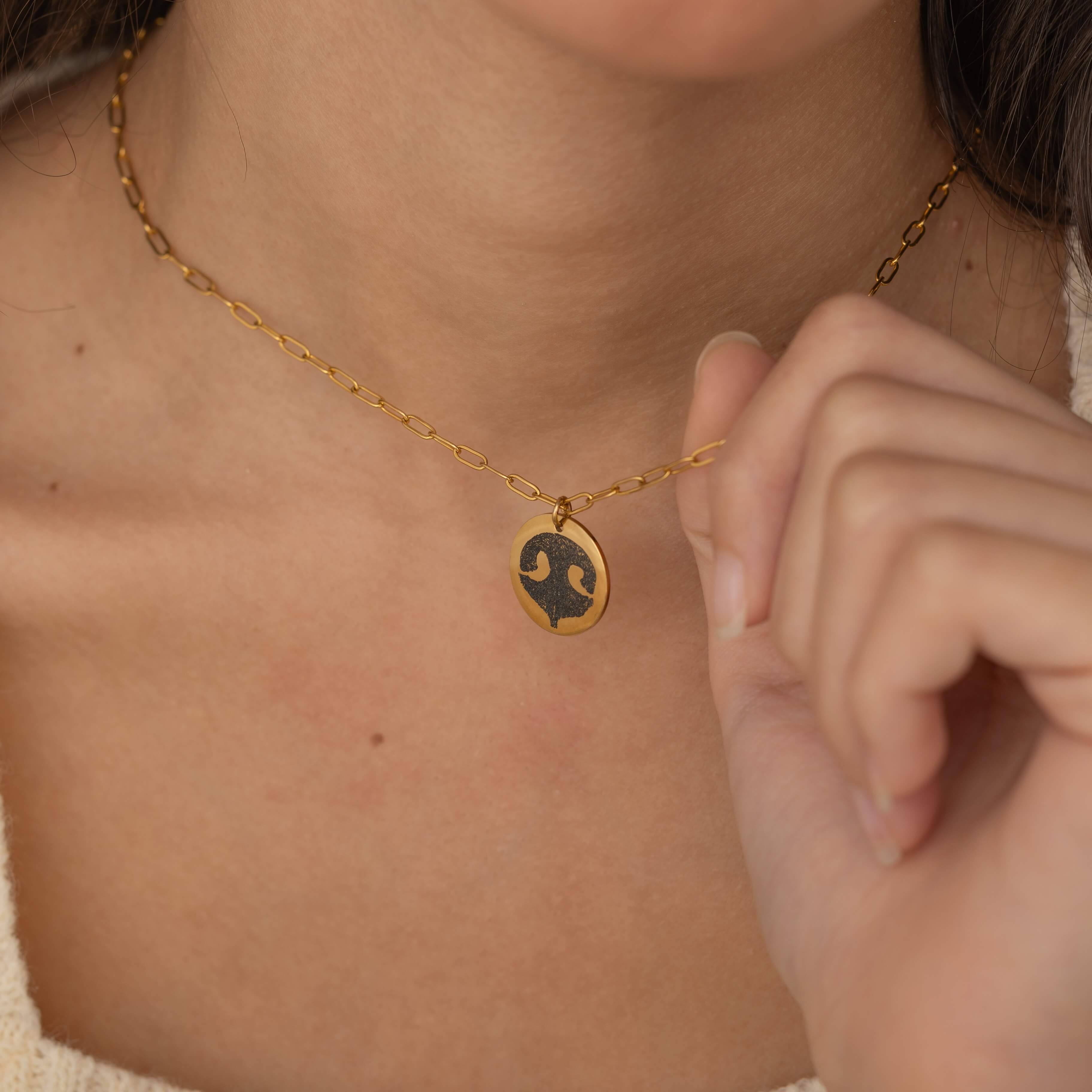 Close-up of a gold pendant necklace featuring an engraved dog nose print design worn by a woman.