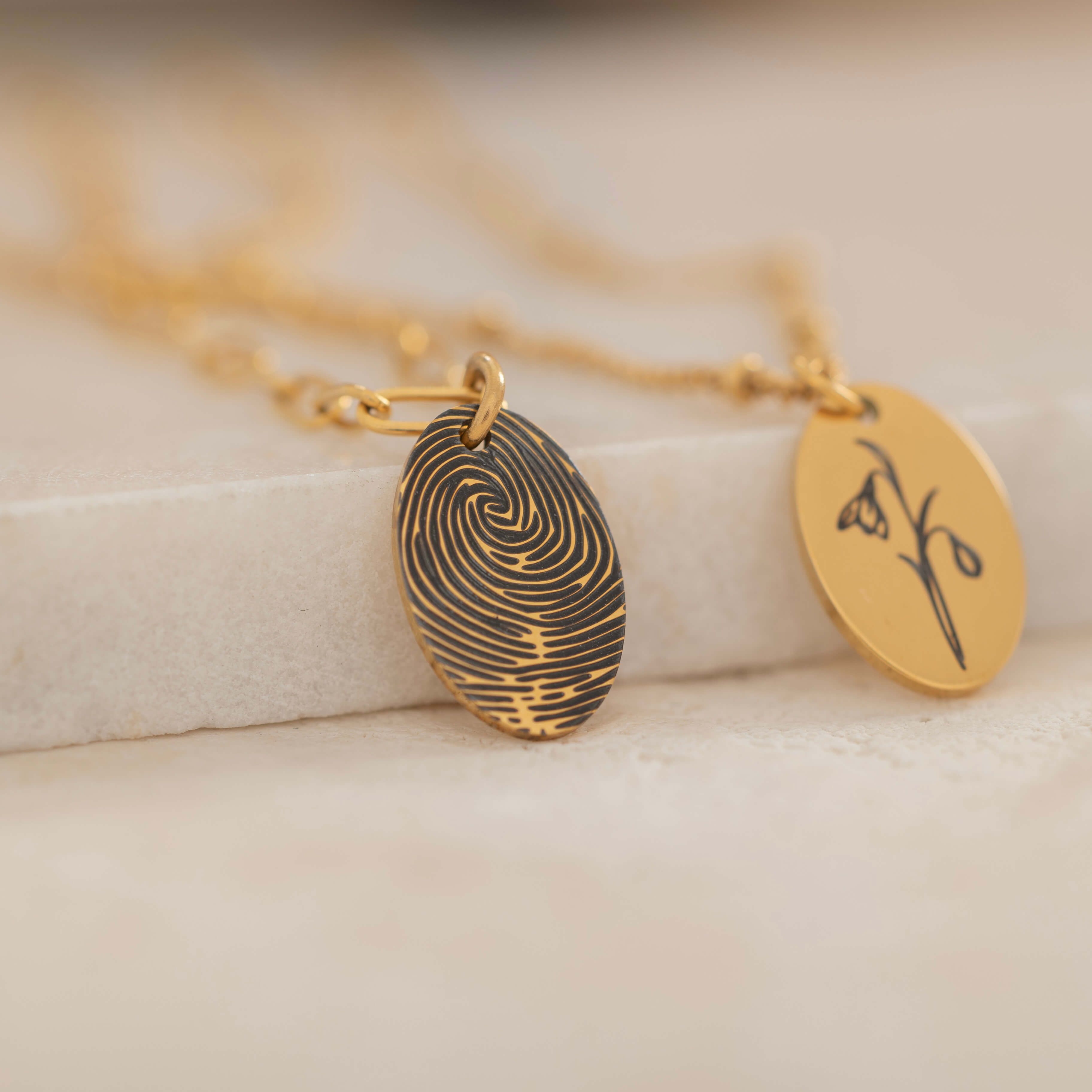 Close-up of a gold pendant engraved with a fingerprint on the front, customizable with a birth flower on the back.