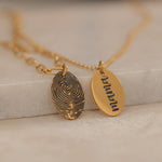 Close-up of a gold pendant engraved with a fingerprint on the front, customizable with a text on the back.