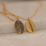 Close-up of a gold pendant engraved with a fingerprint on the front, customizable with a text on the back.