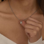 Close-up of a silver pendant necklace featuring an engraved outline of the state of Florida worn by a woman.