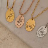 Four engraved necklaces with hand gesture designs, including peace signs and hand-holding, displayed on a marble background.