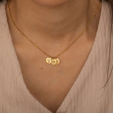 Close-up of a gold custom birth flower engraved pendant necklace worn by a woman, showcasing three round charms with floral engravings being held between fingers.