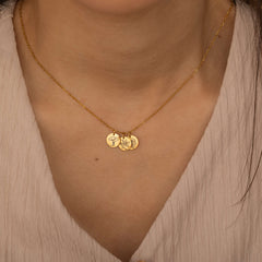 Close-up of a gold custom birth flower engraved pendant necklace worn by a woman, showcasing three round charms with floral engravings being held between fingers.