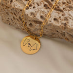 Close-up of a gold pendant necklace engraved with two state outlines and a heart in the center.