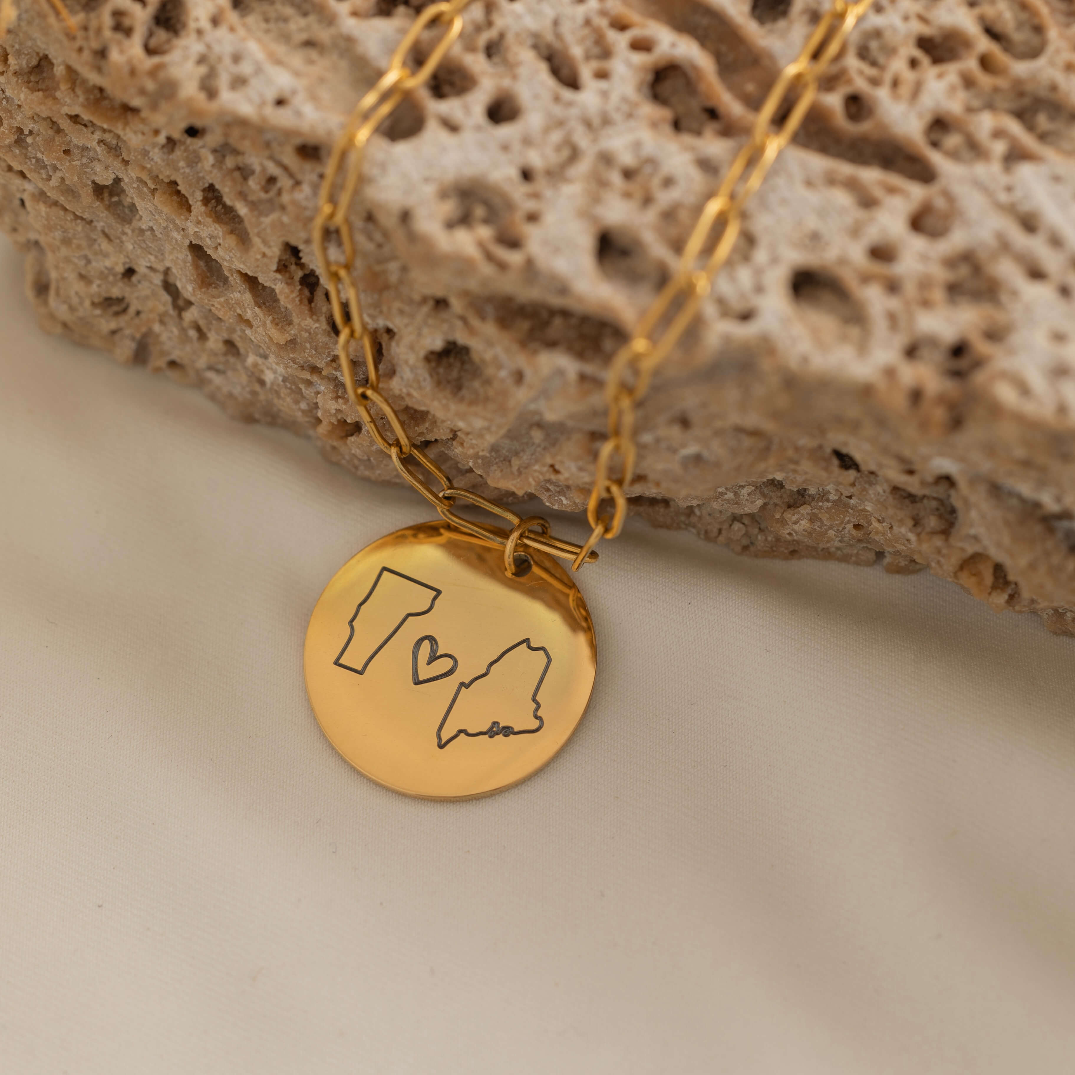 Close-up of a gold pendant necklace engraved with two state outlines and a heart in the center.