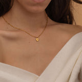 Close-up of a gold pendant necklace with an engraved initial "k" worn by a woman.