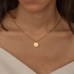 Close-up of a gold pendant necklace with an engraved outline of a US state, worn by a woman.