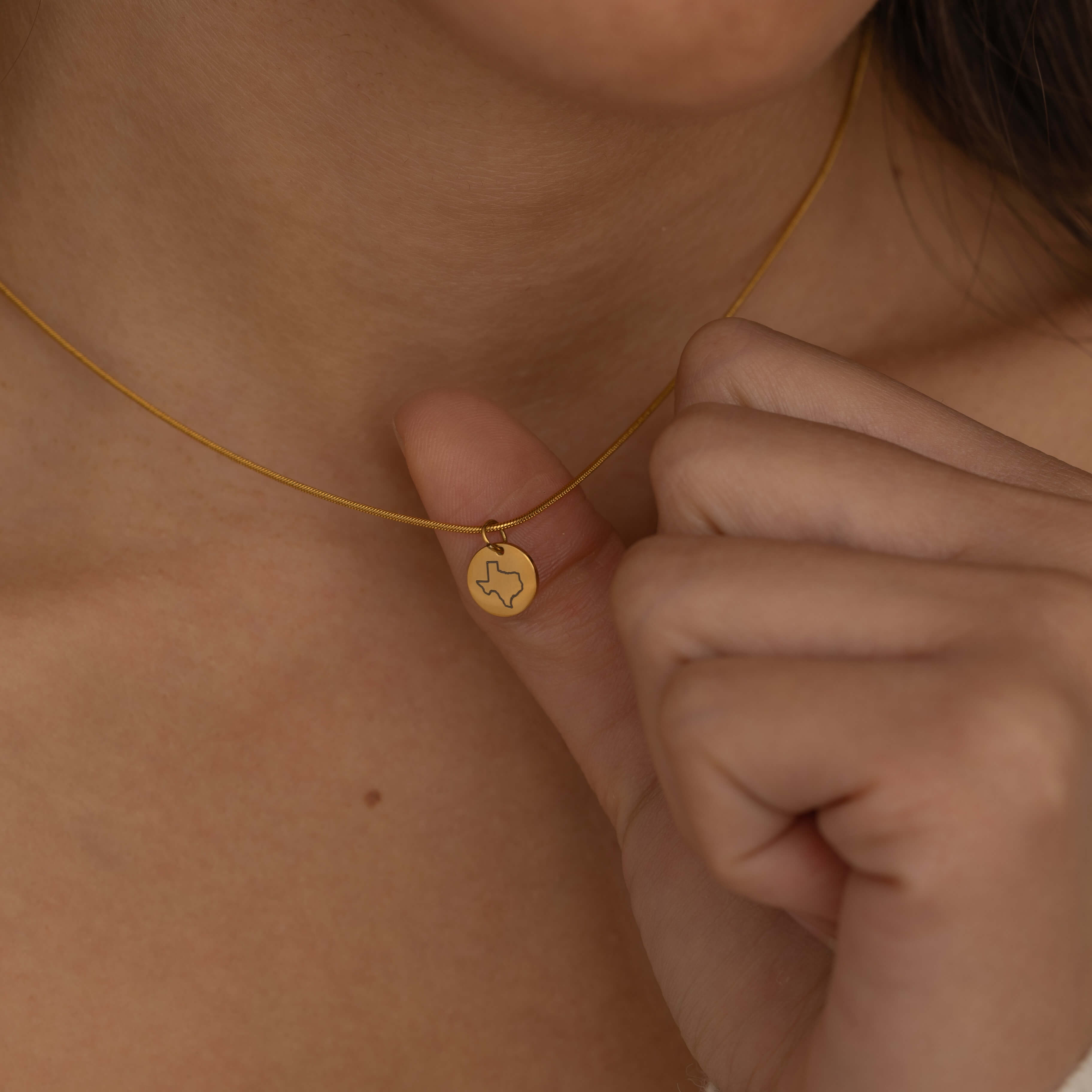 Close-up of a gold pendant necklace featuring an engraved outline of the state of Texas worn by a woman.