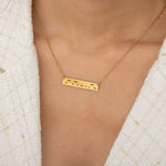 Close-up of a gold bar necklace engraved with a personalized Morse code message, worn by a woman.