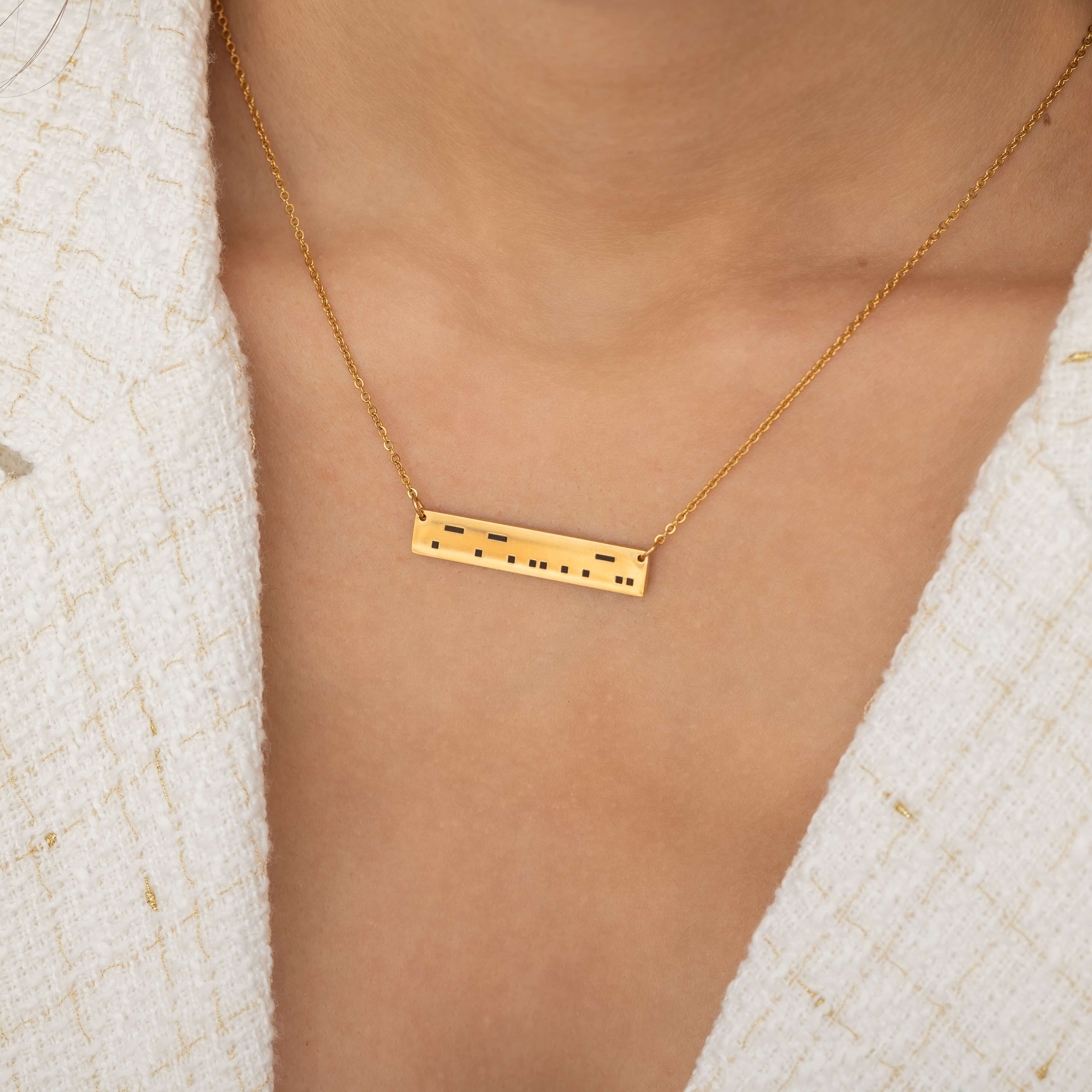 Close-up of a gold bar necklace engraved with a personalized Morse code message, worn by a woman.