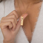 Close-up of a gold pendant necklace featuring an engraved birth flower with a personalized name as the stem, worn by a woman.