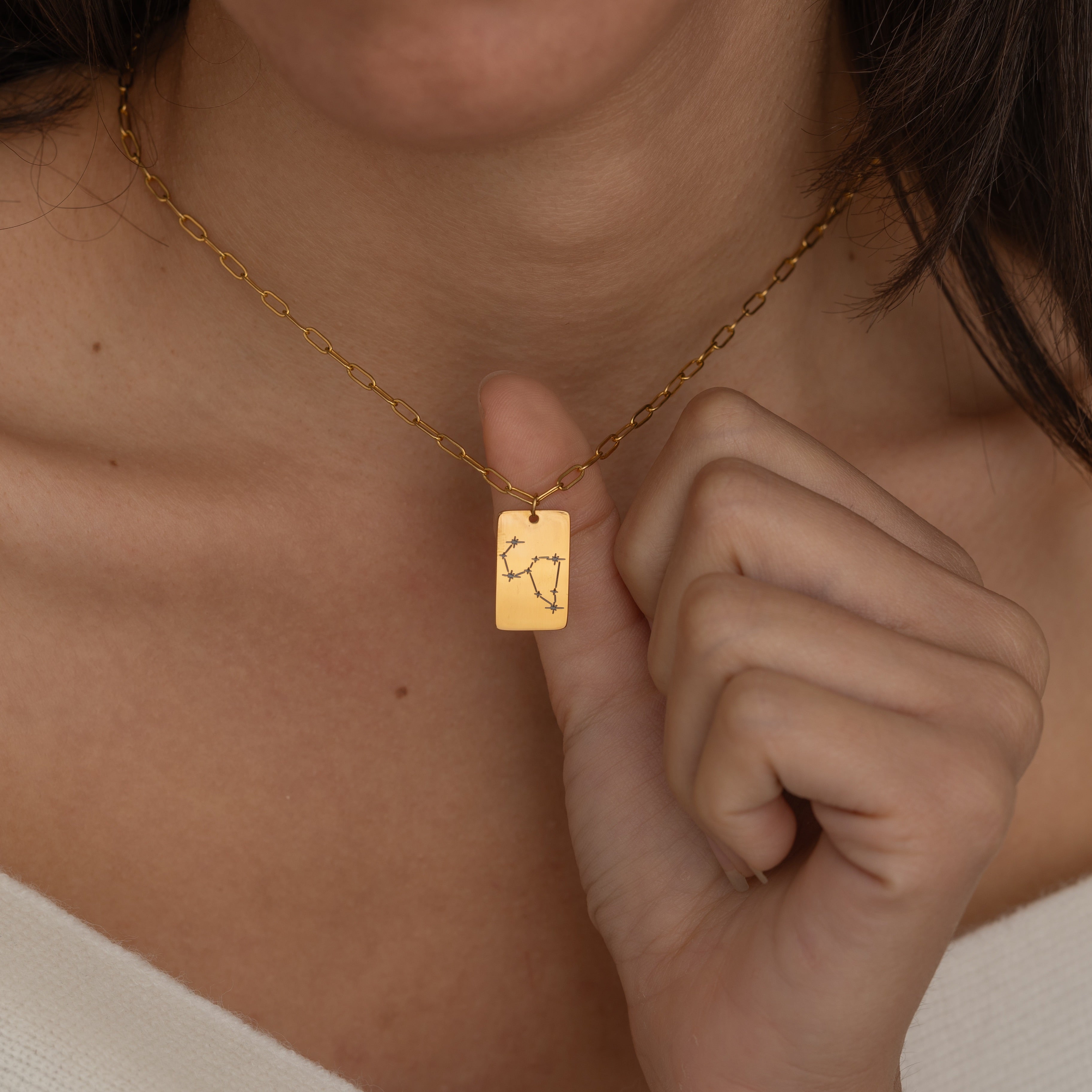 Close-up of a constellation necklace pendant worn by a woman, showcasing a minimalist engraved star pattern.