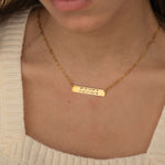 Close-up of a pendant necklace engraved with coordinates worn by a woman.
