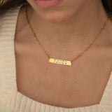 Close-up of a pendant necklace engraved with coordinates worn by a woman.