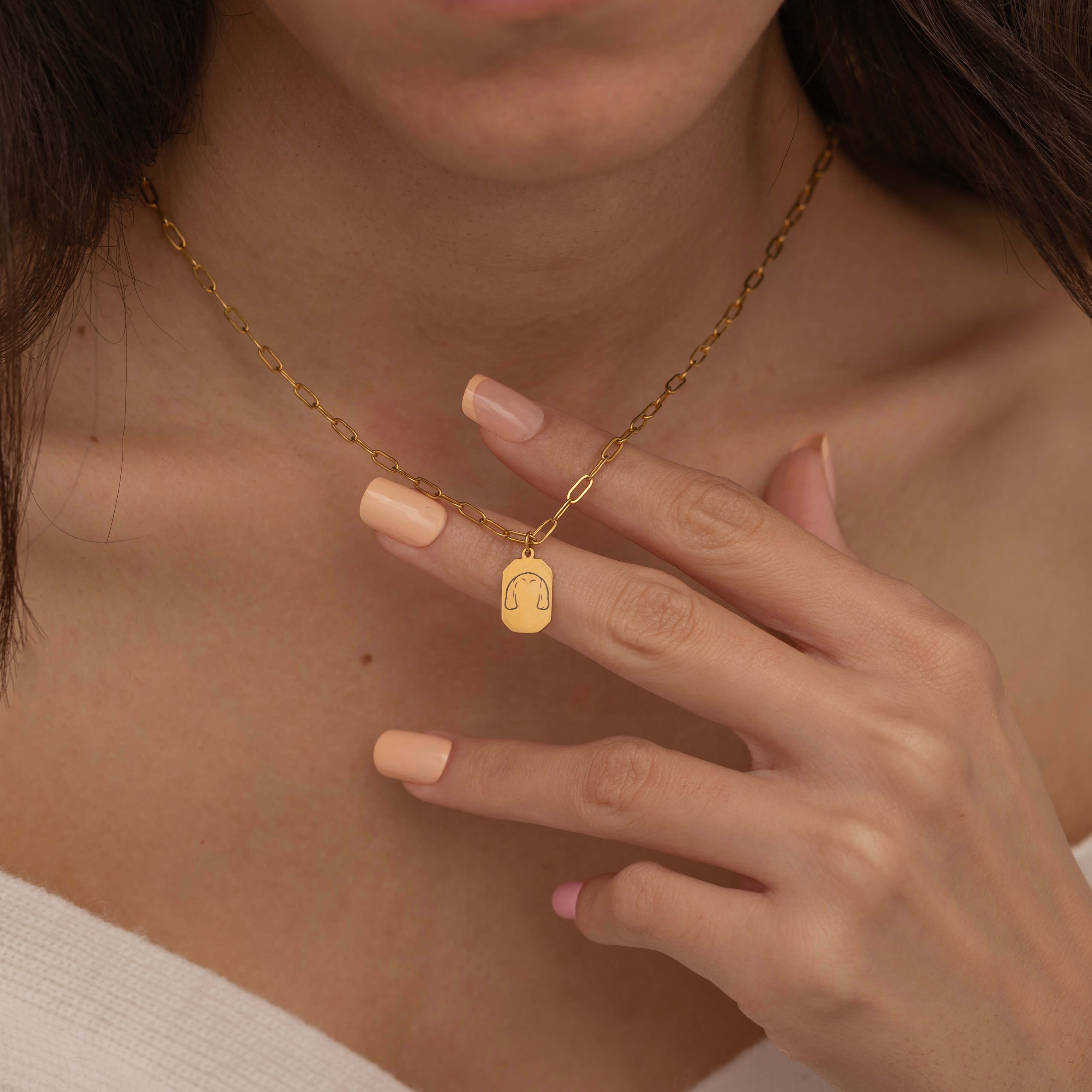Close-up of a gold pendant necklace engraved with a dog's ear outline, worn by a woman.