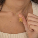 Gold pendant necklace featuring an engraved outline of dog ears with a pet's name underneath, worn by a woman.