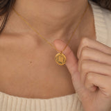 Gold pendant necklace featuring an engraved outline of dog ears with a pet's name underneath, worn by a woman.