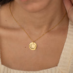 Gold pendant necklace featuring an engraved outline of dog ears with a pet's name underneath, worn by a woman.