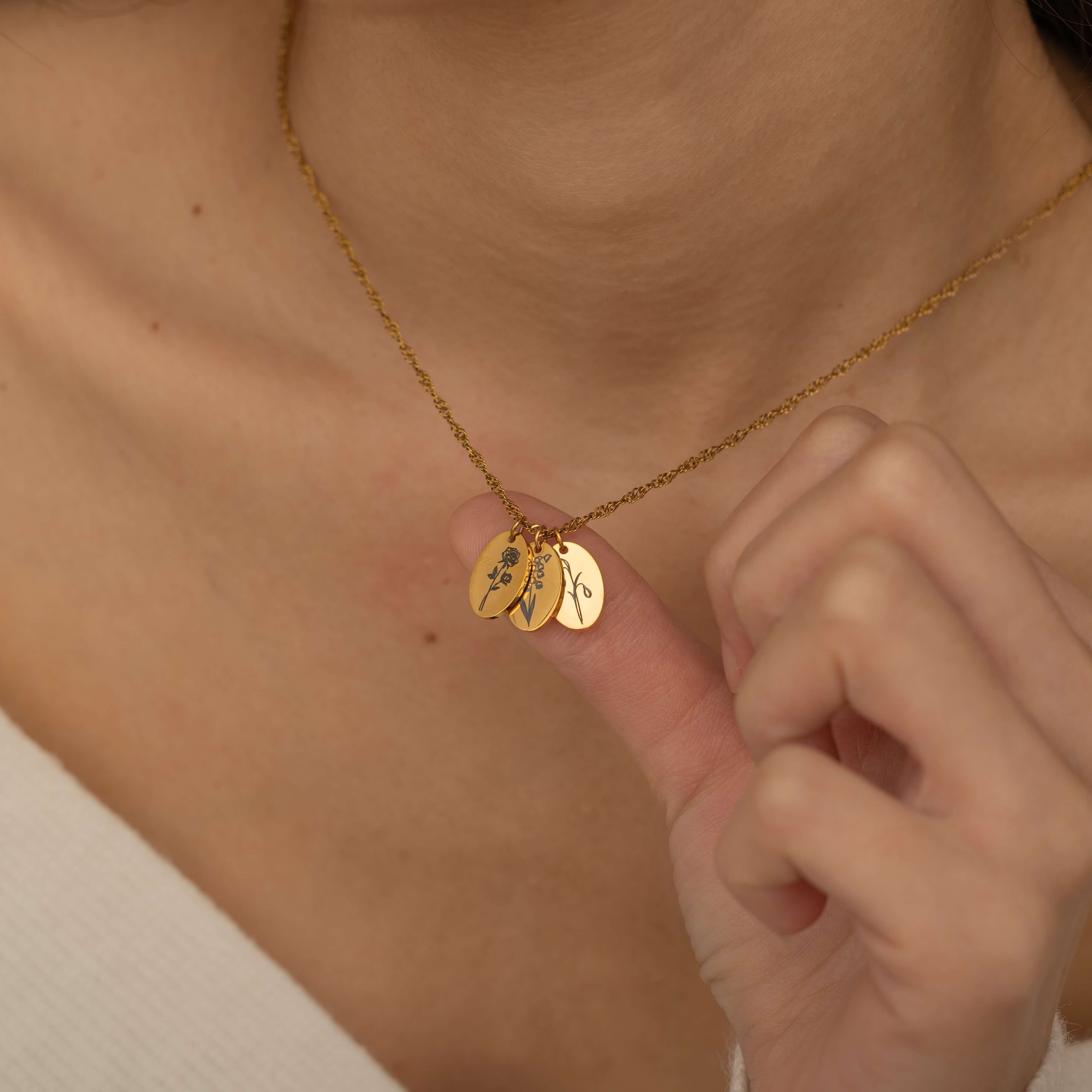 Close-up of a gold necklace with multiple pendants, each engraved with a birth flower representing different family members, worn by a woman.