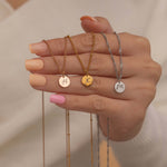 Close-up of a rose gold, gold and silver pendant necklaces with engraved initial letters held by a women hand