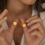 Gold necklace with multiple charms, each engraved with different US state outlines and heart, worn by a woman.