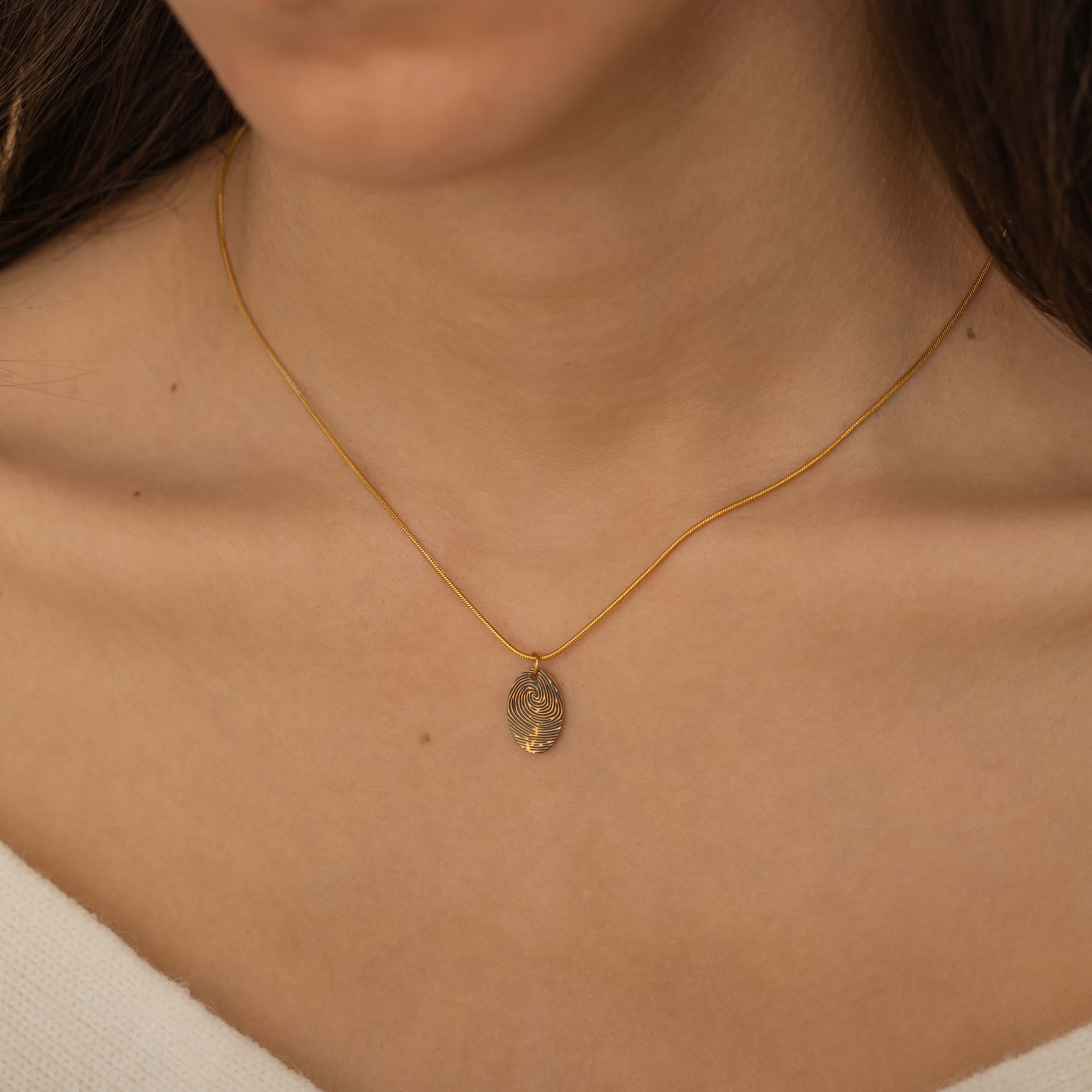 Close-up of a gold pendant engraved with a fingerprint on the front, customizable with a birth flower or text on the back, worn by a woman.