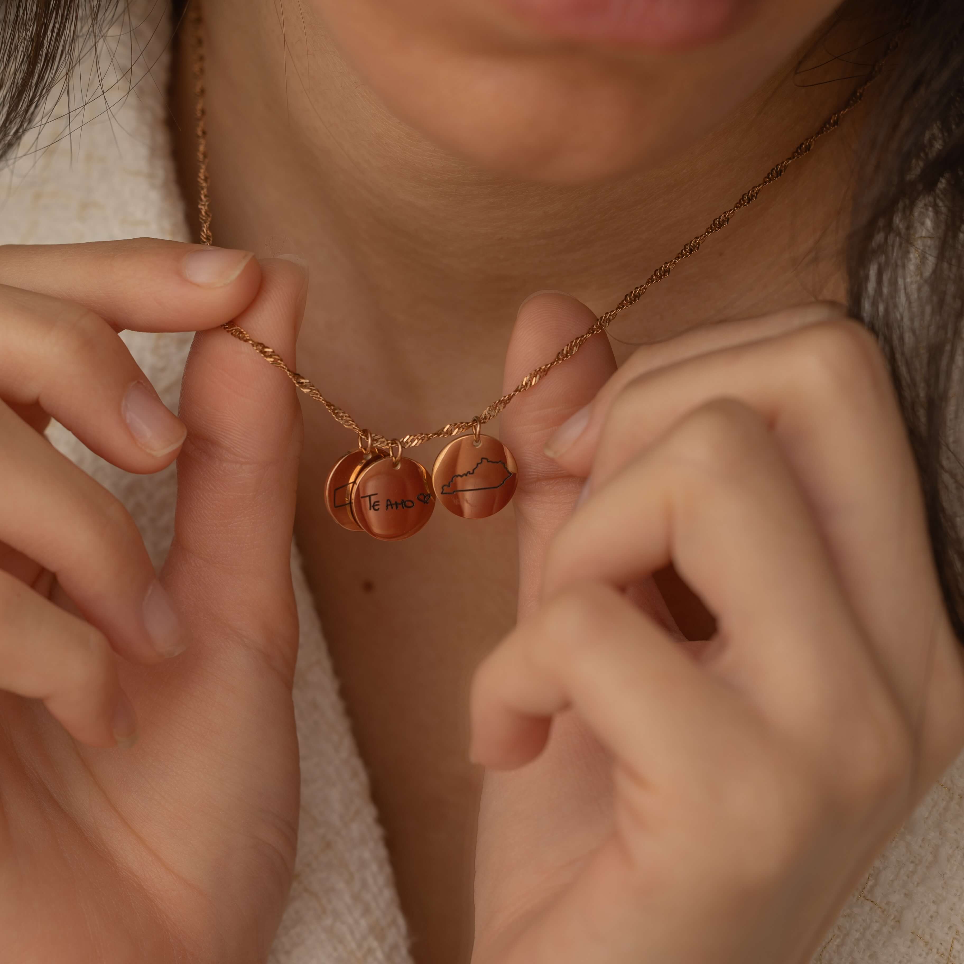 Rose Gold necklace with multiple charms, each engraved with different US state outlines and personalized message, worn by a woman.