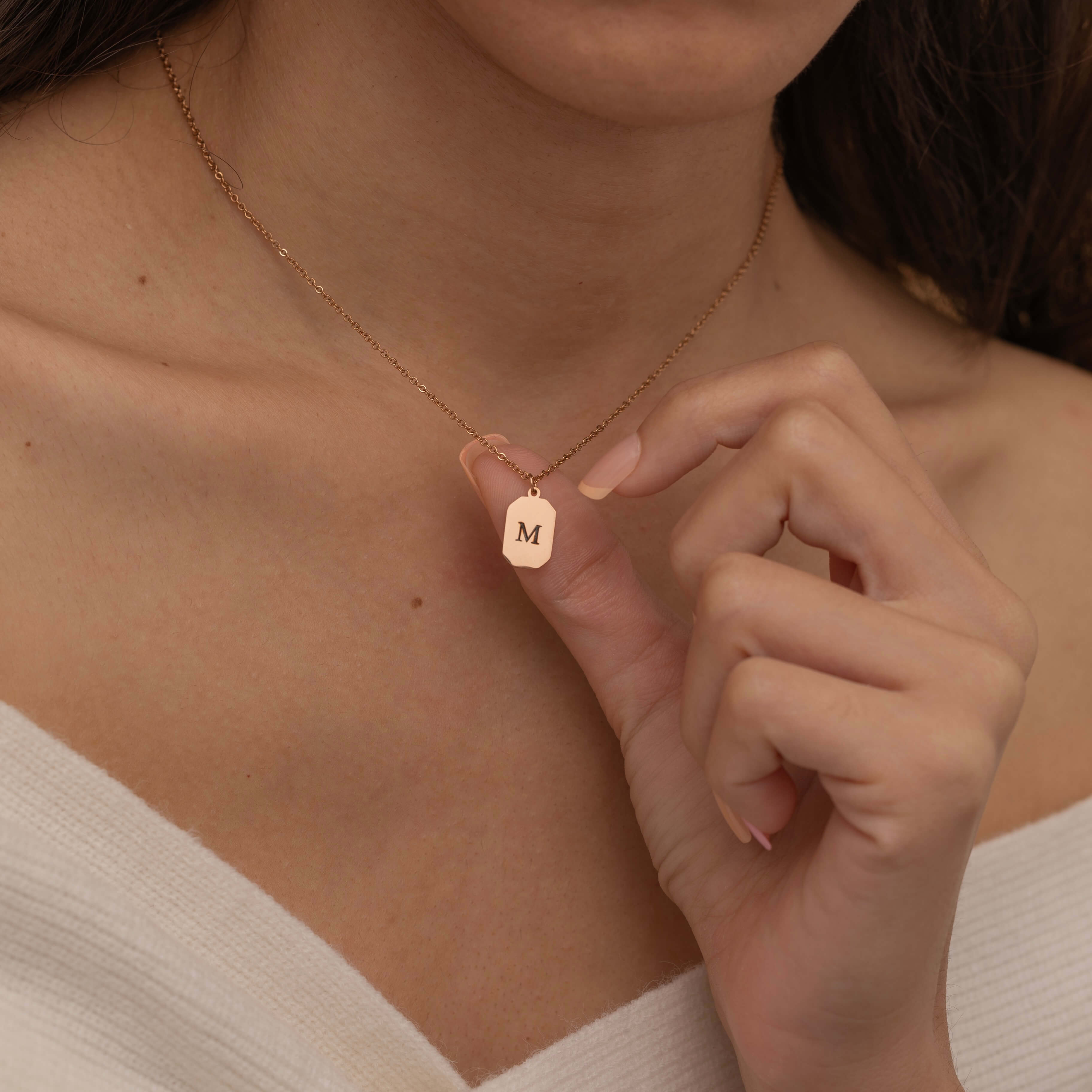 Close-up of a rose gold pendant necklace engraved with the letter "M," worn by a woman.