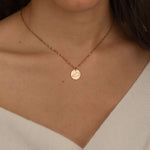 Close-up of a rose gold pendant necklace with an engraved outline of a US state, worn by a woman.