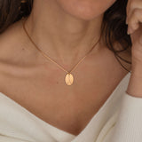 Close-up of a rose gold pendant necklace featuring an engraved zodiac constellation design worn by a women.