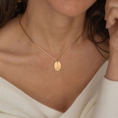 Close-up of a rose gold pendant necklace featuring an engraved zodiac constellation design worn by a women.