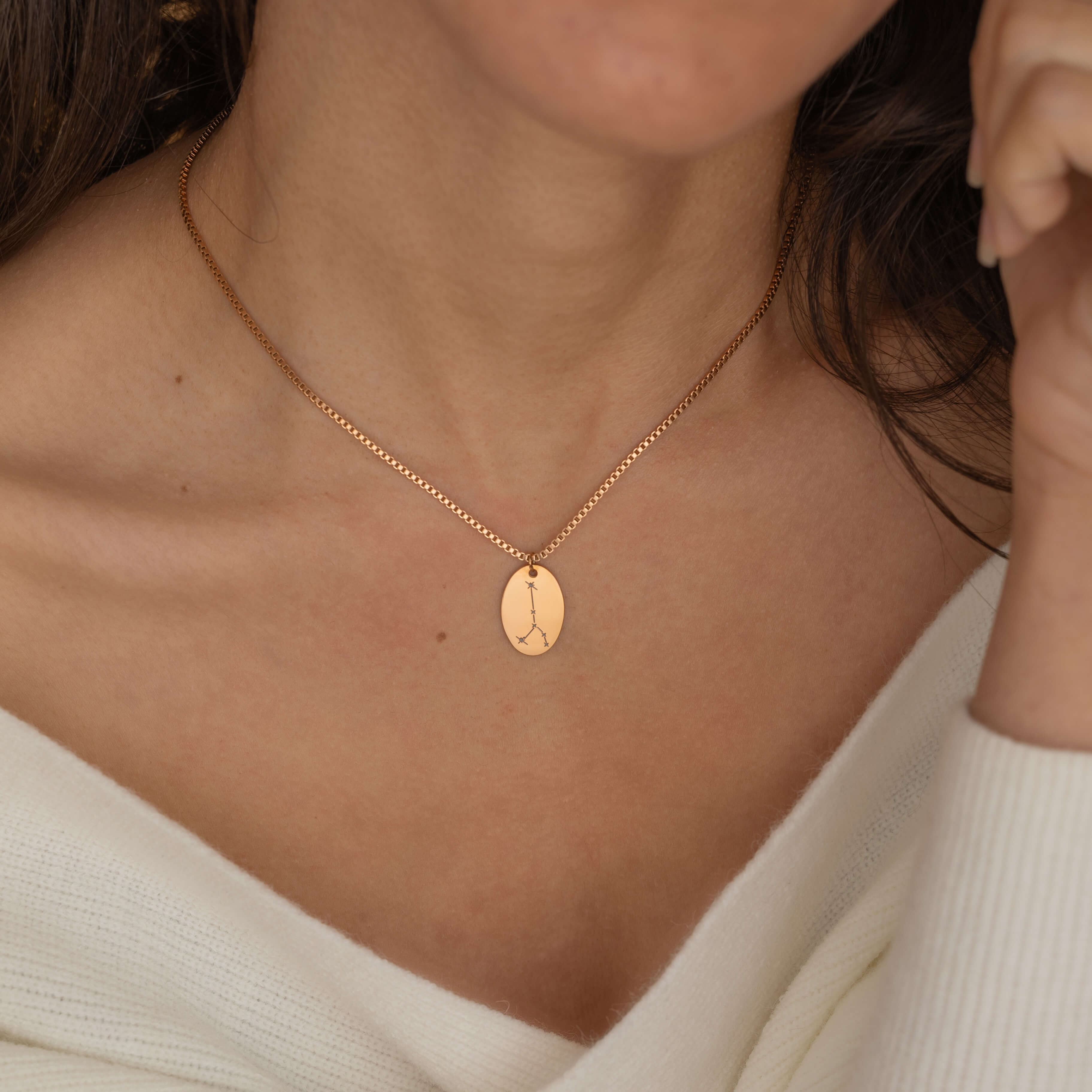Close-up of a rose gold pendant necklace featuring an engraved zodiac constellation design worn by a women.