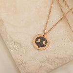 Close-up of a rose gold pendant necklace featuring an engraved dog nose print design on top of a stone.