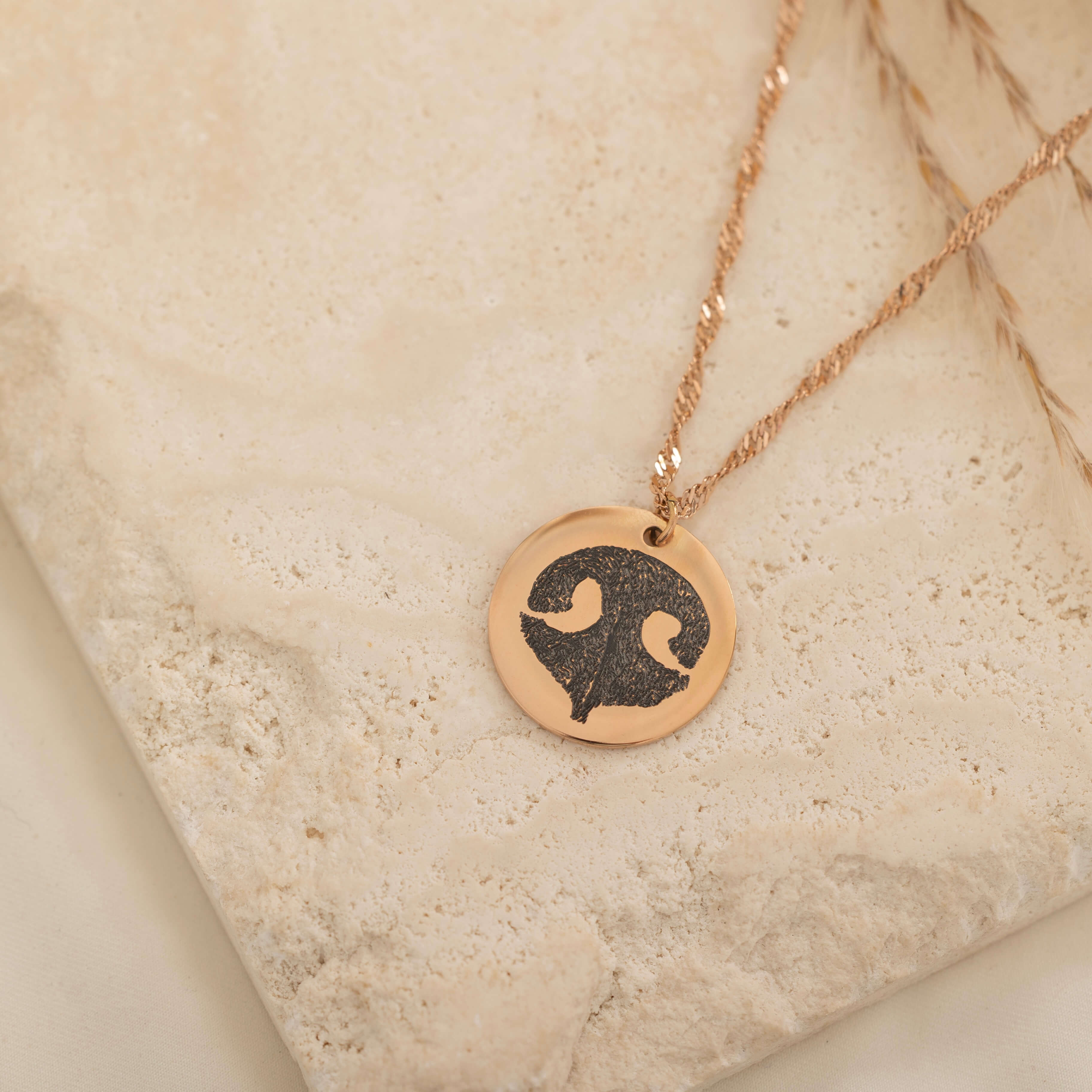 Close-up of a rose gold pendant necklace featuring an engraved dog nose print design on top of a stone.