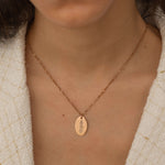 Close-up of a rose gold pendant necklace featuring a personalized engraving of a plant leaf design worn by a women.