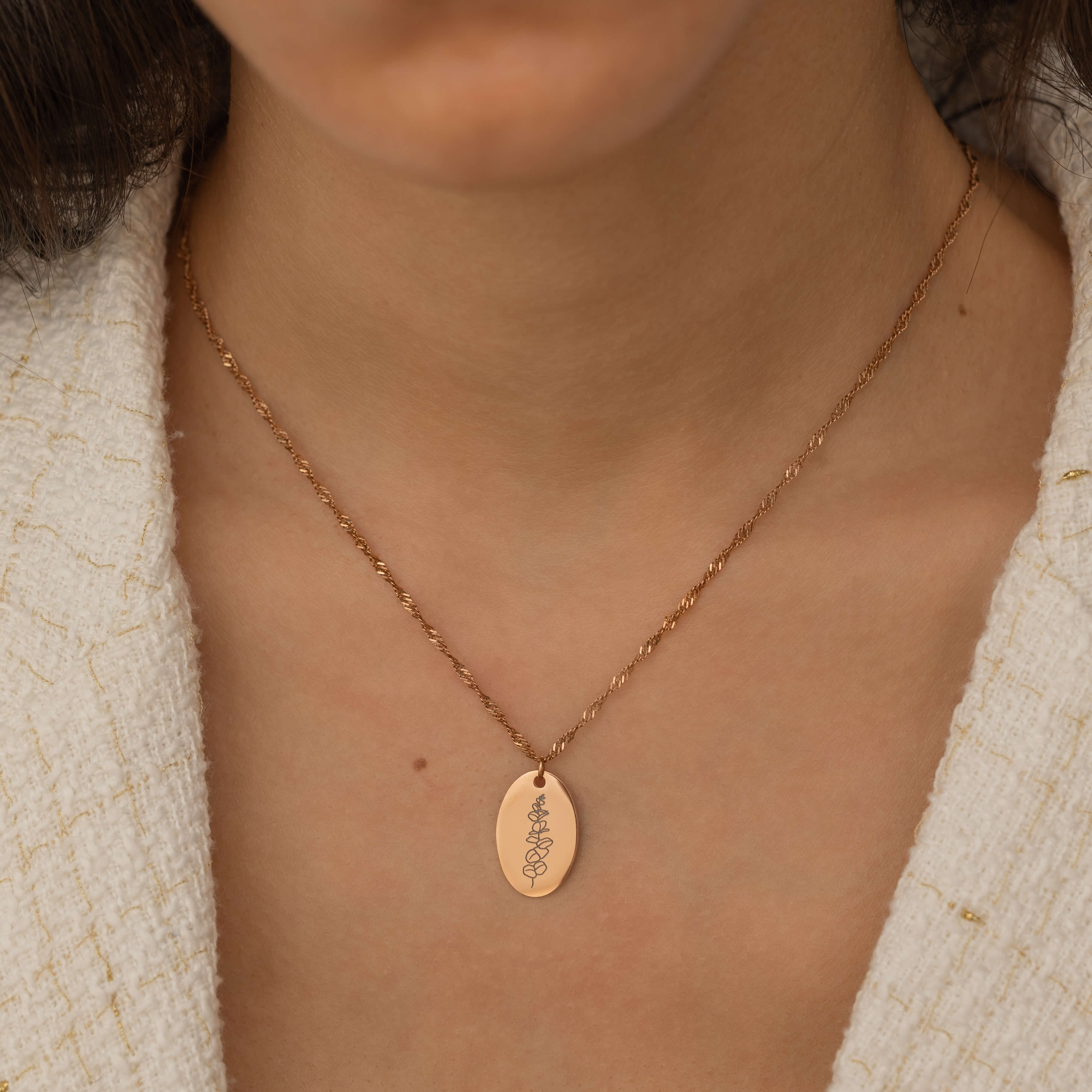 Close-up of a rose gold pendant necklace featuring a personalized engraving of a plant leaf design worn by a women.