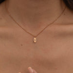 Close-up of a rose gold necklace with engraved pendant, featuring an initial, worn by a woman.