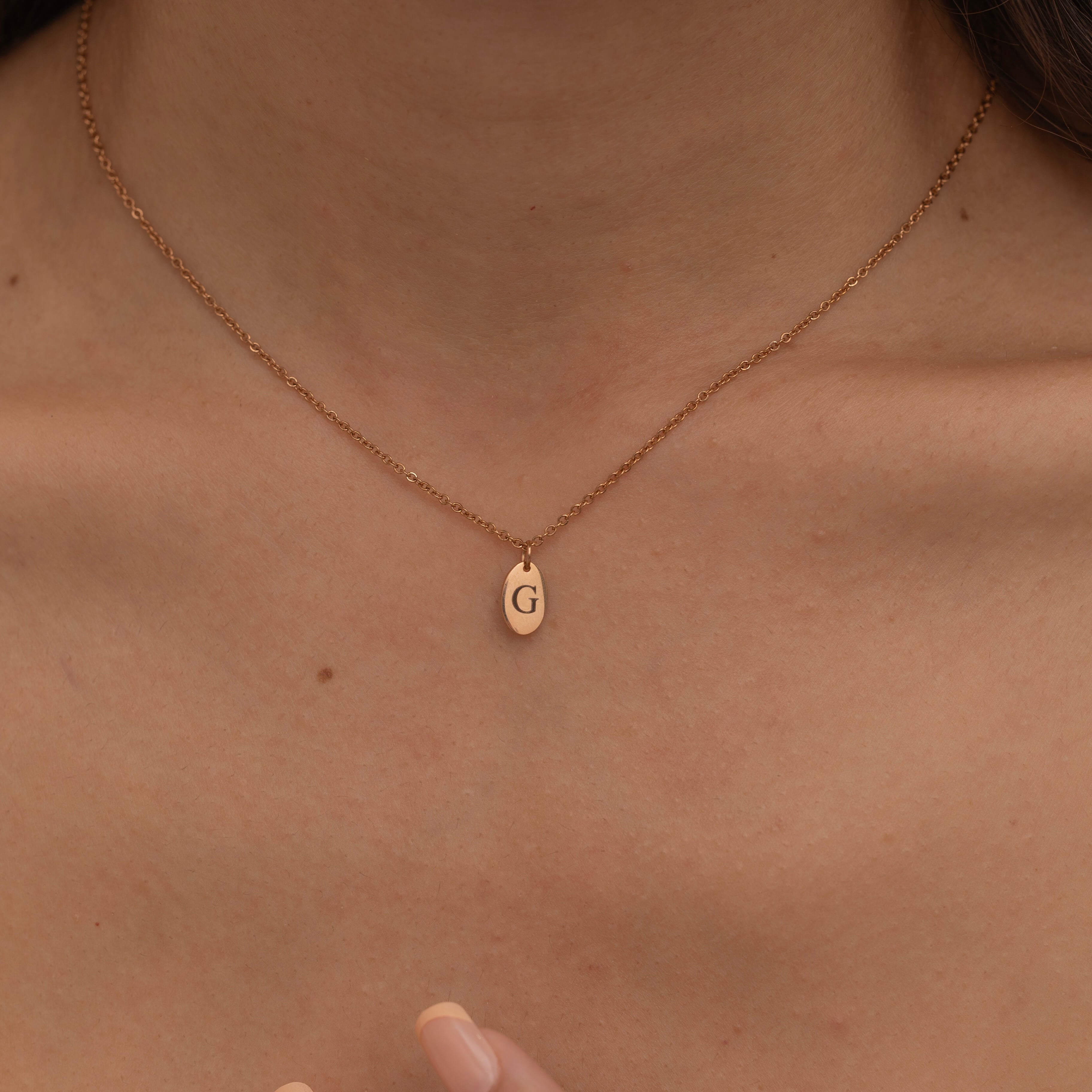 Close-up of a rose gold necklace with engraved pendant, featuring an initial, worn by a woman.