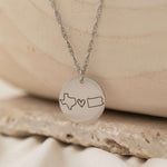 Close-up of a silver pendant necklace engraved with two state outlines and a heart in the center.