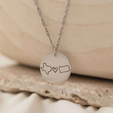 Close-up of a silver pendant necklace engraved with two state outlines and a heart in the center.