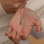 Close-up of a silver pendant necklace with an engraved initial "m" held by a woman hand