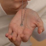 Close-up of a silver pendant necklace with an engraved initial "m" held by a woman hand
