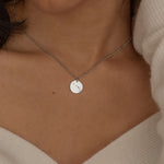 Close-up of a silver pendant necklace with an engraved outline of a US state, worn by a woman.