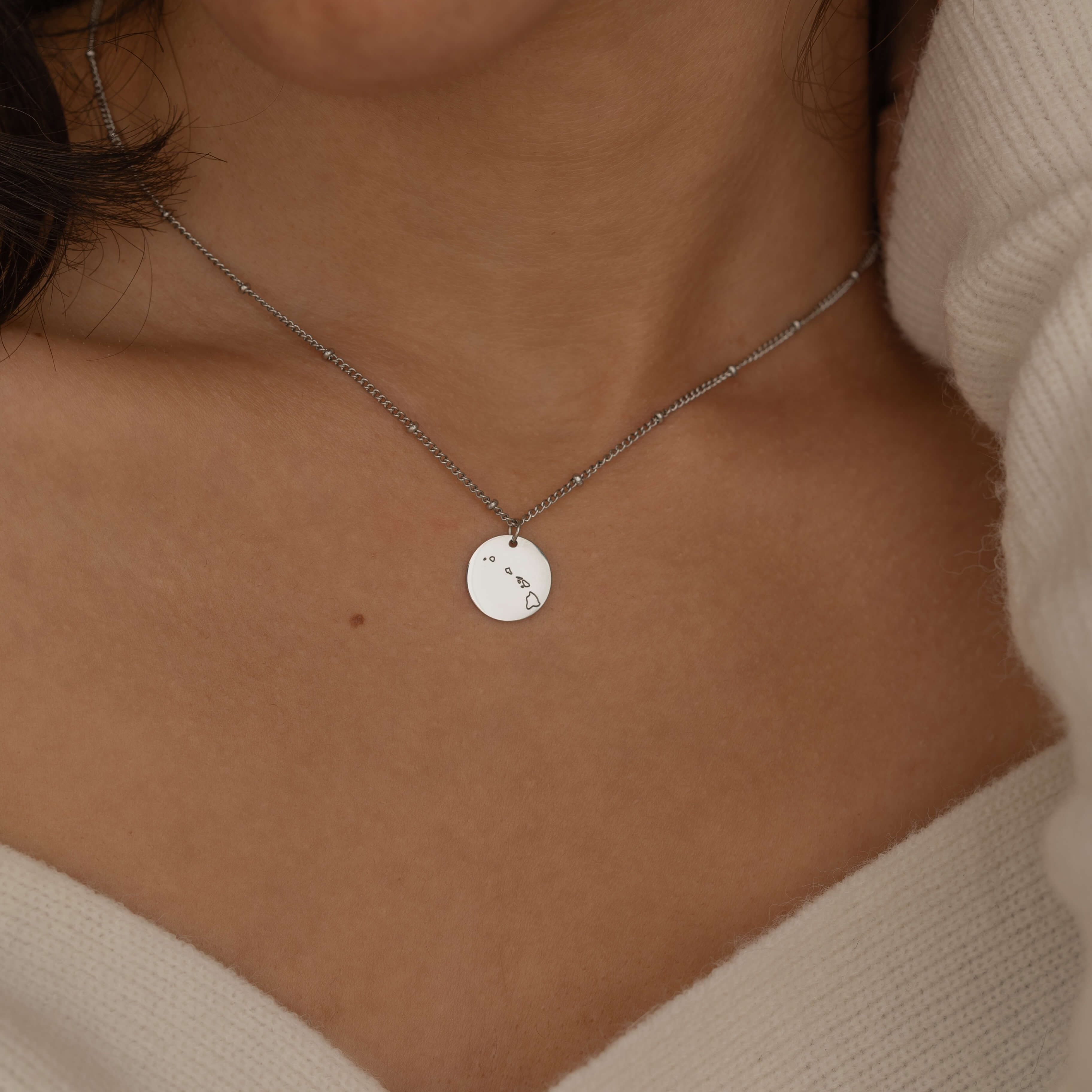 Close-up of a silver pendant necklace with an engraved outline of a US state, worn by a woman.