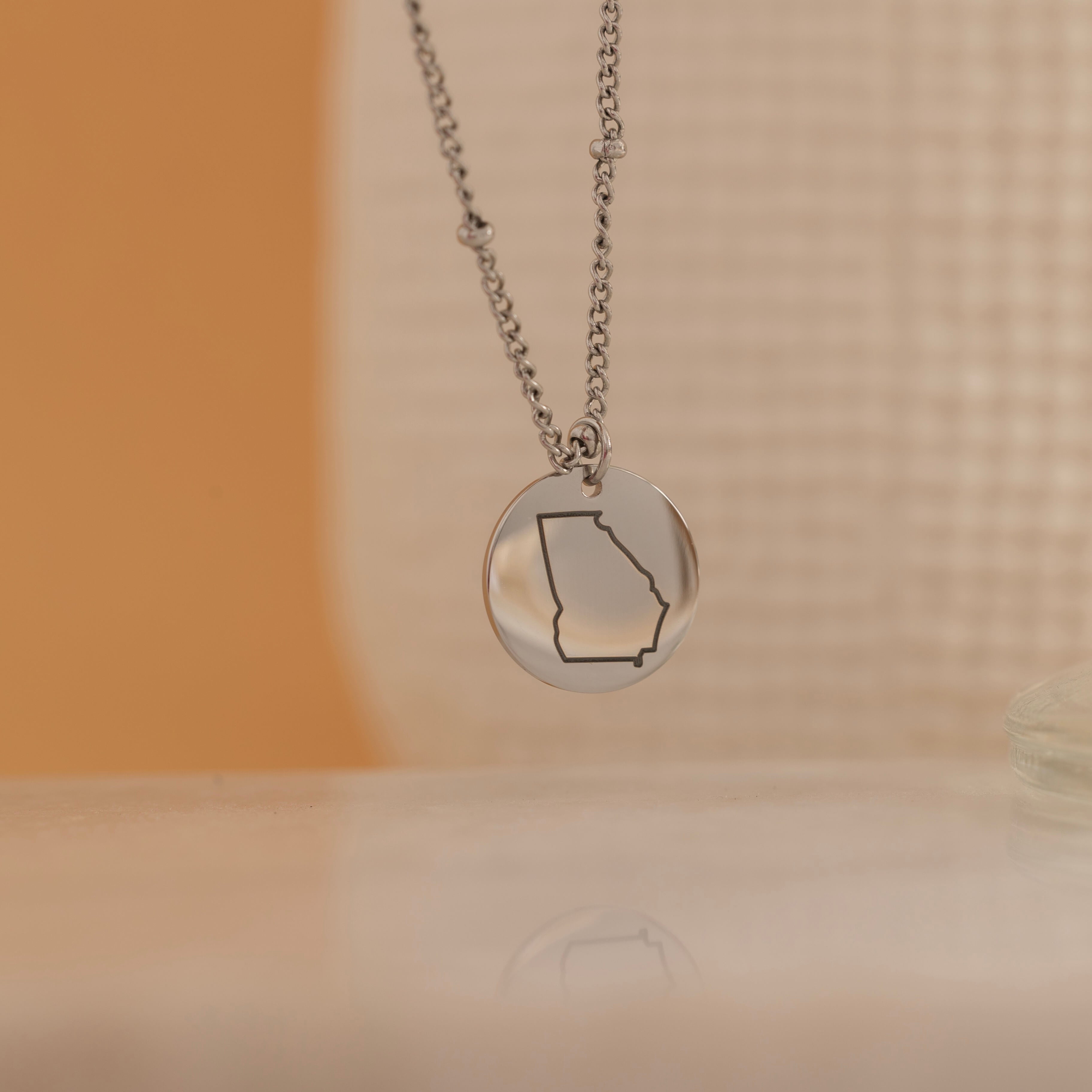 Silver necklace of a US State outline hanging 
